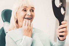 An older woman admiring her dentures while looking in a hand mirror