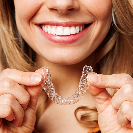 Woman smiling while holding clear aligner